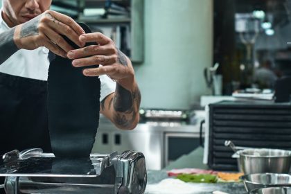 Traditional italian food. Cropped image of chef's hands with tattoos rolling a black dough